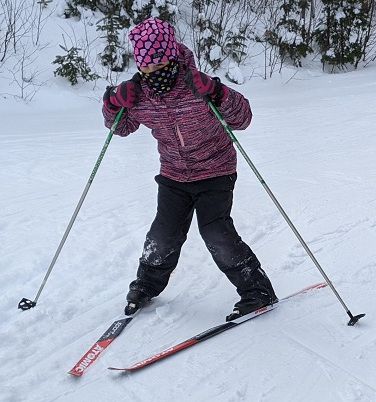A child learning to snowplow on cross-country skis