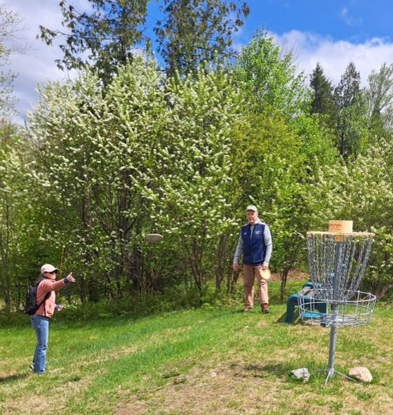 Two players on the course in spring, one mid-throw, flowering trees behind them